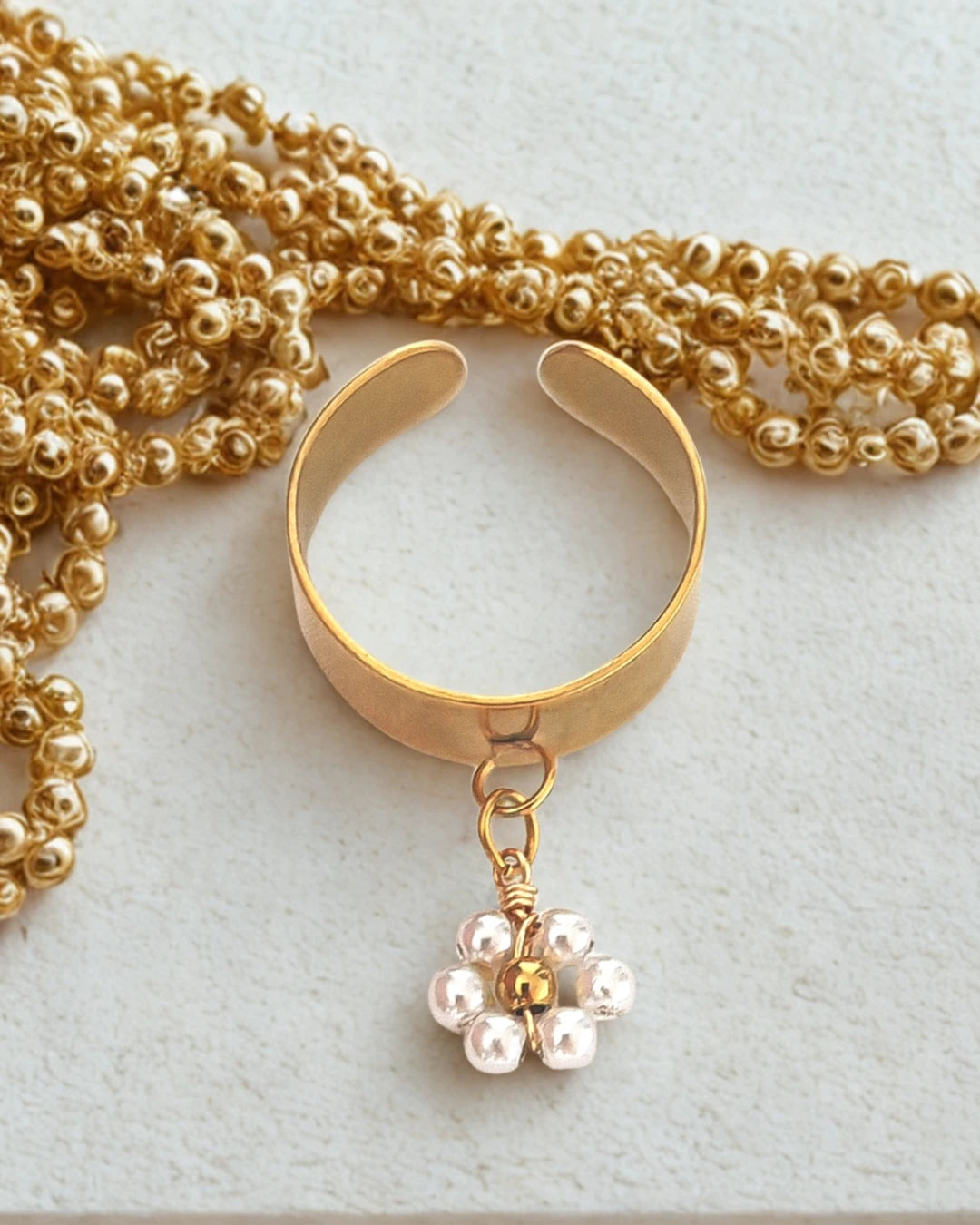 Élégante et délicate, cette bague dorée ajustable est sublimée par un pendentif en forme de fleur composée de petites perles nacrées. Un bijou plein de charme et de douceur, qui capture la lumière et symbolise la féminité sous toutes ses formes.