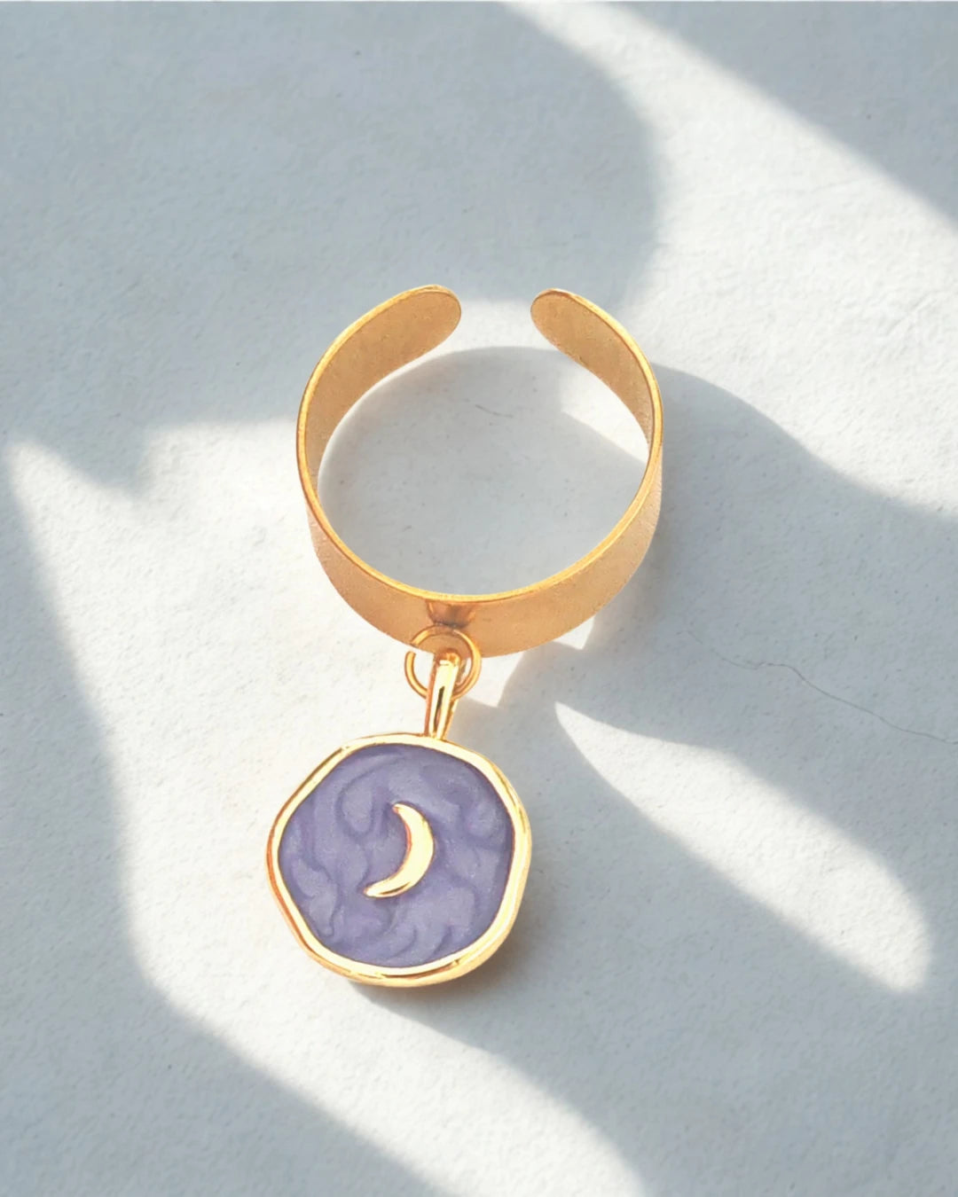 Laissez-vous séduire par cette bague dorée ornée d’un pendentif rond émaillé violet et d’un motif lune dorée. Elle incarne la féminité, la douceur et la magie du ciel nocturne. Son design raffiné et symbolique en fait un bijou plein de charme et d’énergie positive.