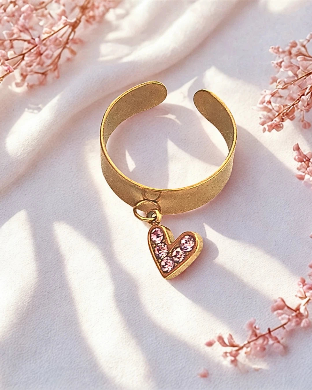 Un bijou tout en douceur pour célébrer l’amour et la féminité. Cette bague dorée ajustable est sublimée par un pendentif en forme de cœur, orné de cristaux roses étincelants. Raffinée et lumineuse, elle reflète la tendresse et l’élégance à chaque geste.