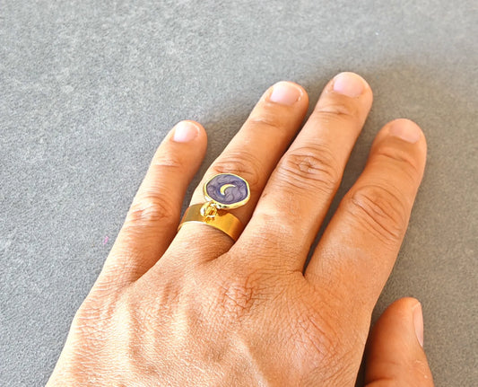 Laissez-vous séduire par cette bague dorée ornée d’un pendentif rond émaillé violet et d’un motif lune dorée. Elle incarne la féminité, la douceur et la magie du ciel nocturne. Son design raffiné et symbolique en fait un bijou plein de charme et d’énergie positive.