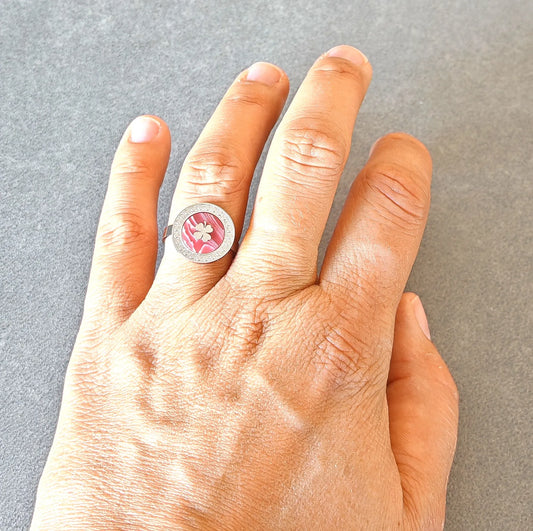 Portez la chance à votre doigt avec cette bague argentée au design raffiné. Son médaillon rond révèle un fond nacré rose doux, orné d’un trèfle délicat, symbole de chance et de positivité. Un bijou à la fois élégant et plein de sens, idéal pour illuminer vos journées.