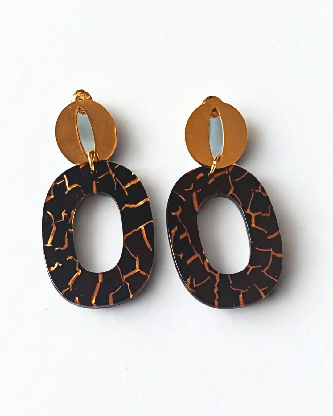 Affirmez votre style avec ces boucles d'oreilles noires et dorées au design géométrique et raffiné. Leur contraste subtil entre l'effet marbré noir aux éclats dorés et la brillance du métal apporte une touche d'élégance contemporaine à toutes vos tenues.