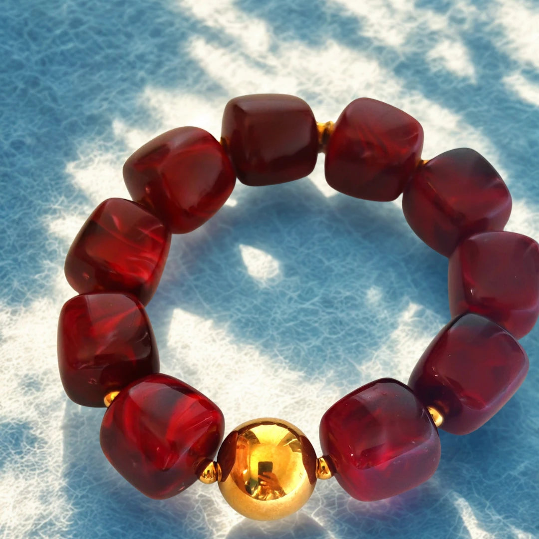 e bracelet audacieux allie modernité et raffinement grâce à ses perles en résine effet pierre, délicatement facettées, et sa perle centrale en acier inoxydable doré. Son design sculptural et lumineux en fait un bijou tendance, parfait pour illuminer vos tenues du quotidien ou vos looks d’été.

Disponible en deux teintes élégantes :

Rouge profond : une nuance vibrante et chaleureuse, symbole de passion et de vitalité.

Prune rosé : une couleur douce et féminine, qui reflète la sérénité et l’élégance.