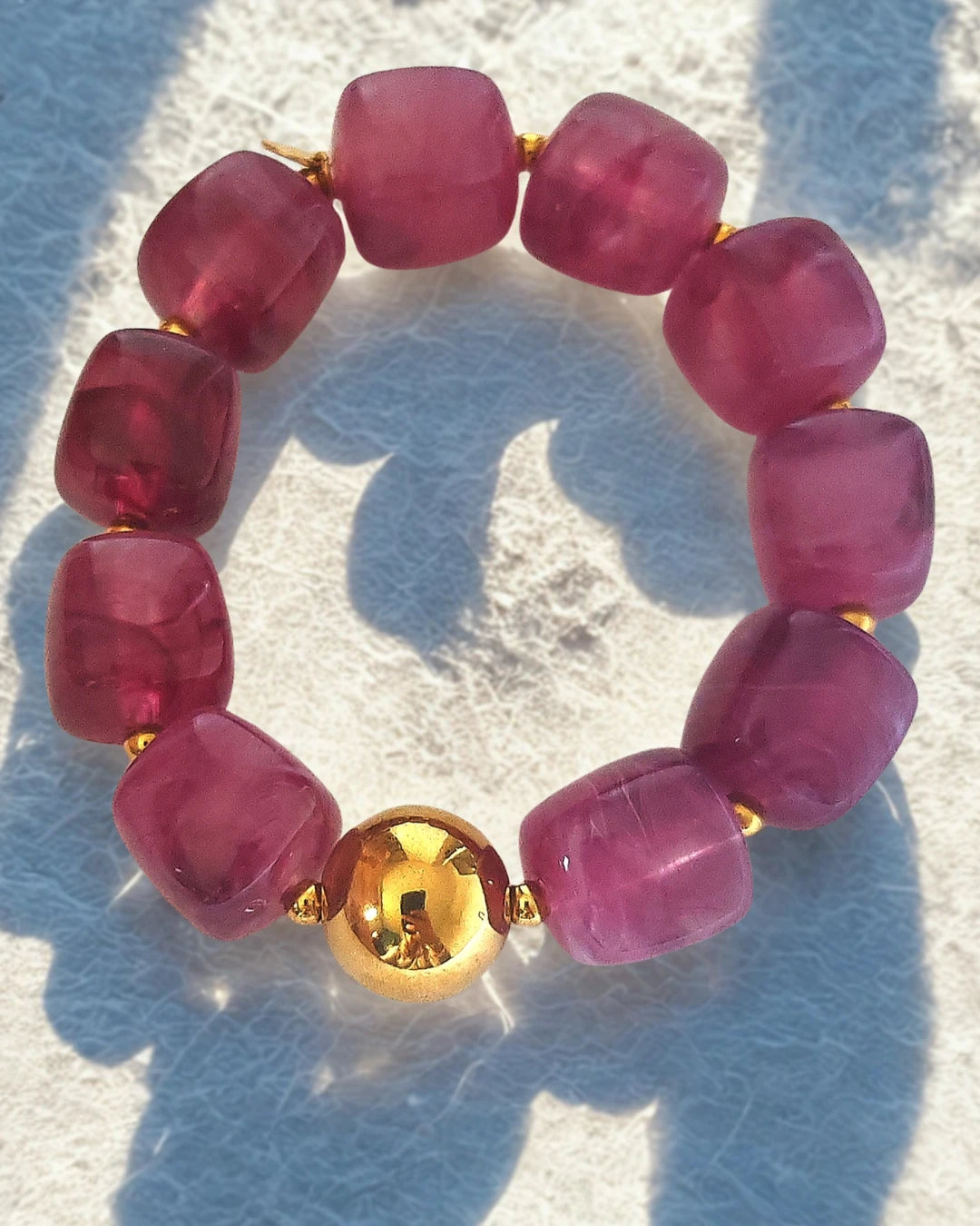 e bracelet audacieux allie modernité et raffinement grâce à ses perles en résine effet pierre, délicatement facettées, et sa perle centrale en acier inoxydable doré. Son design sculptural et lumineux en fait un bijou tendance, parfait pour illuminer vos tenues du quotidien ou vos looks d’été.

Disponible en deux teintes élégantes :

Rouge profond : une nuance vibrante et chaleureuse, symbole de passion et de vitalité.

Prune rosé : une couleur douce et féminine, qui reflète la sérénité et l’élégance.