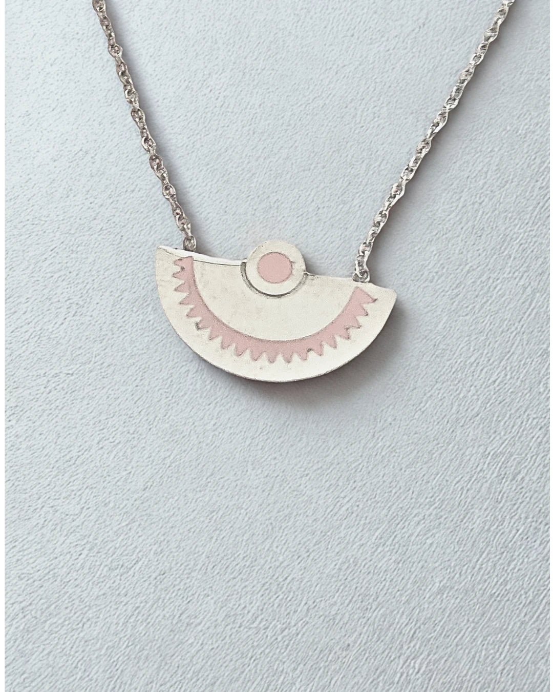 Laissez-vous séduire par l’élégance minimaliste de ce collier demi-lune en acier inoxydable argenté. Son pendentif délicatement gravé aux tons rosés évoque la douceur et l’équilibre, pour un bijou à la fois moderne et symbolique.