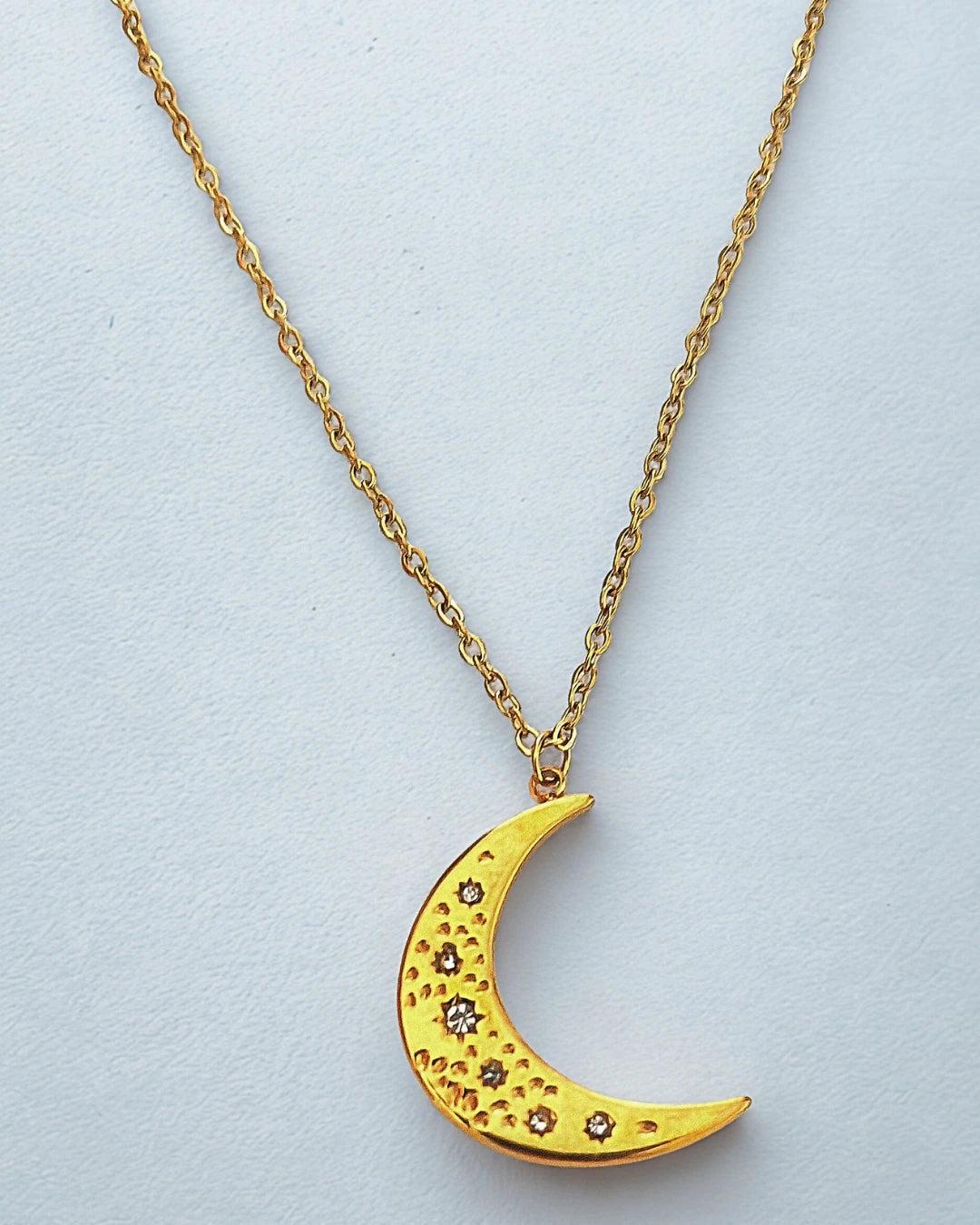 Succombez à la magie de ce collier doré orné d’un pendentif en forme de lune délicatement gravée. Symbole de féminité et de renouveau, il capte la lumière avec subtilité et apporte une touche d’éclat mystique à votre style.