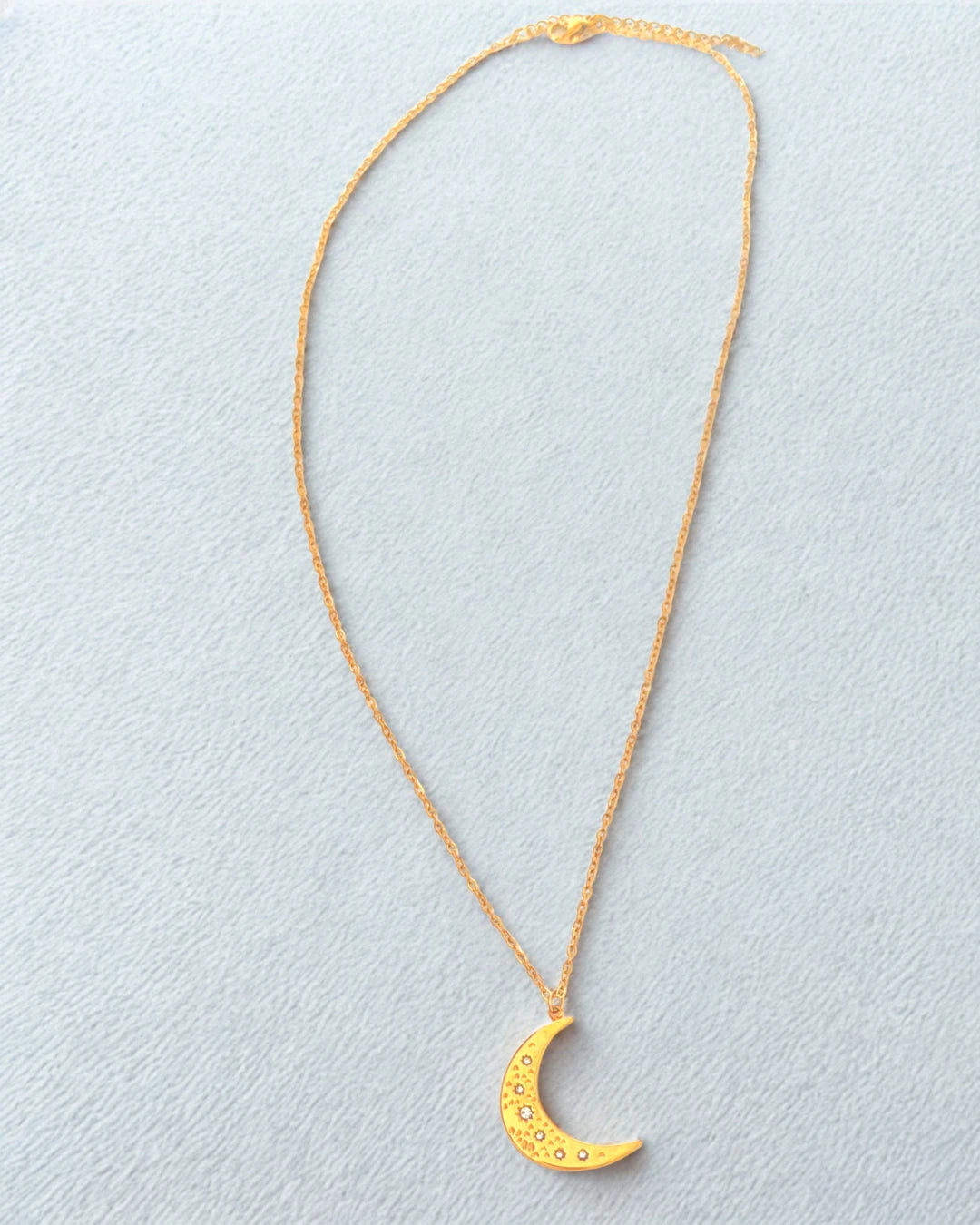 Succombez à la magie de ce collier doré orné d’un pendentif en forme de lune délicatement gravée. Symbole de féminité et de renouveau, il capte la lumière avec subtilité et apporte une touche d’éclat mystique à votre style.
