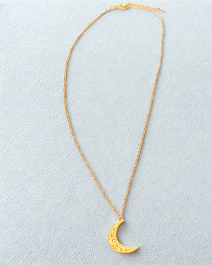 Succombez à la magie de ce collier doré orné d’un pendentif en forme de lune délicatement gravée. Symbole de féminité et de renouveau, il capte la lumière avec subtilité et apporte une touche d’éclat mystique à votre style.