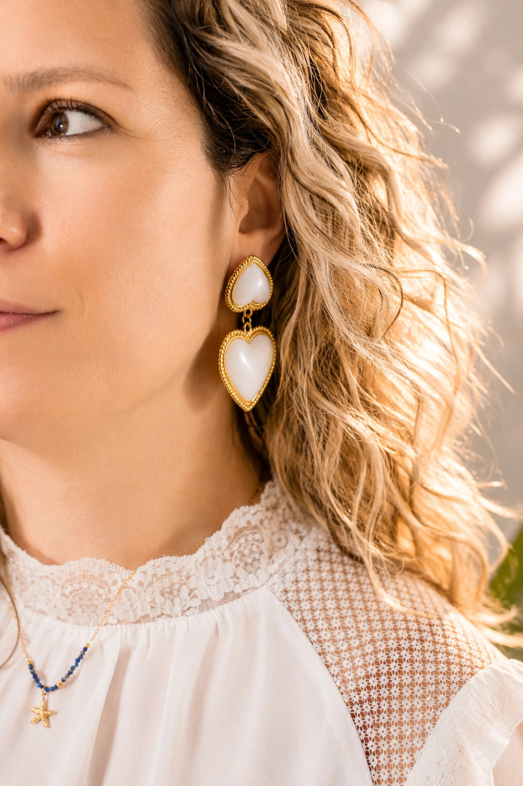 Boucles d’oreilles cœur blanc nacré et doré portées par une femme