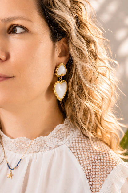 Boucles d’oreilles cœur blanc nacré et doré portées par une femme