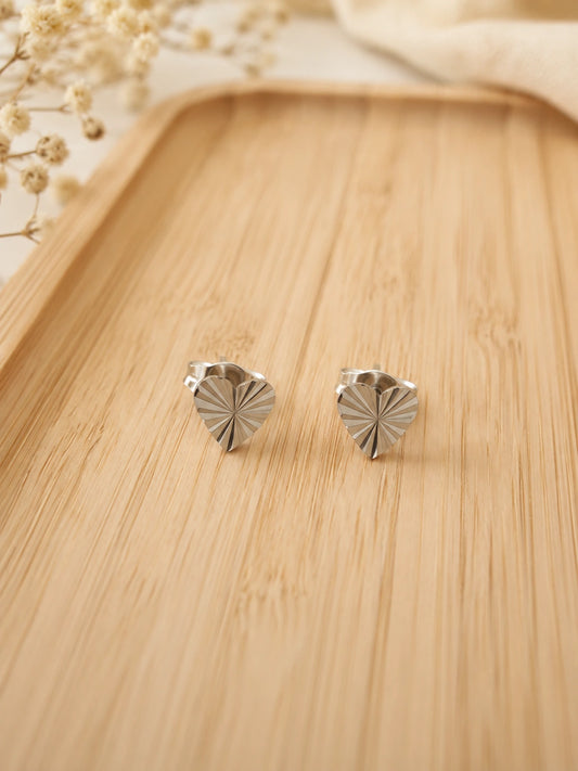 Boucles d’oreilles petit cœur argenté en acier inoxydable sur fond bois clair