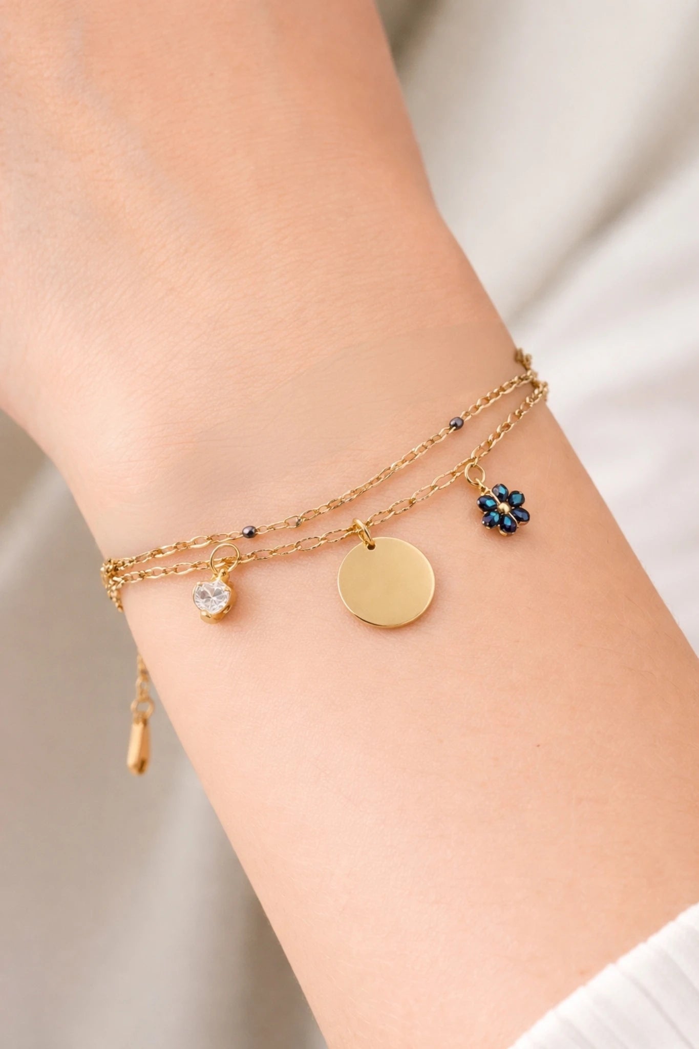 Bracelet double chaîne doré porté au poignet avec médaille gravable et charms scintillants