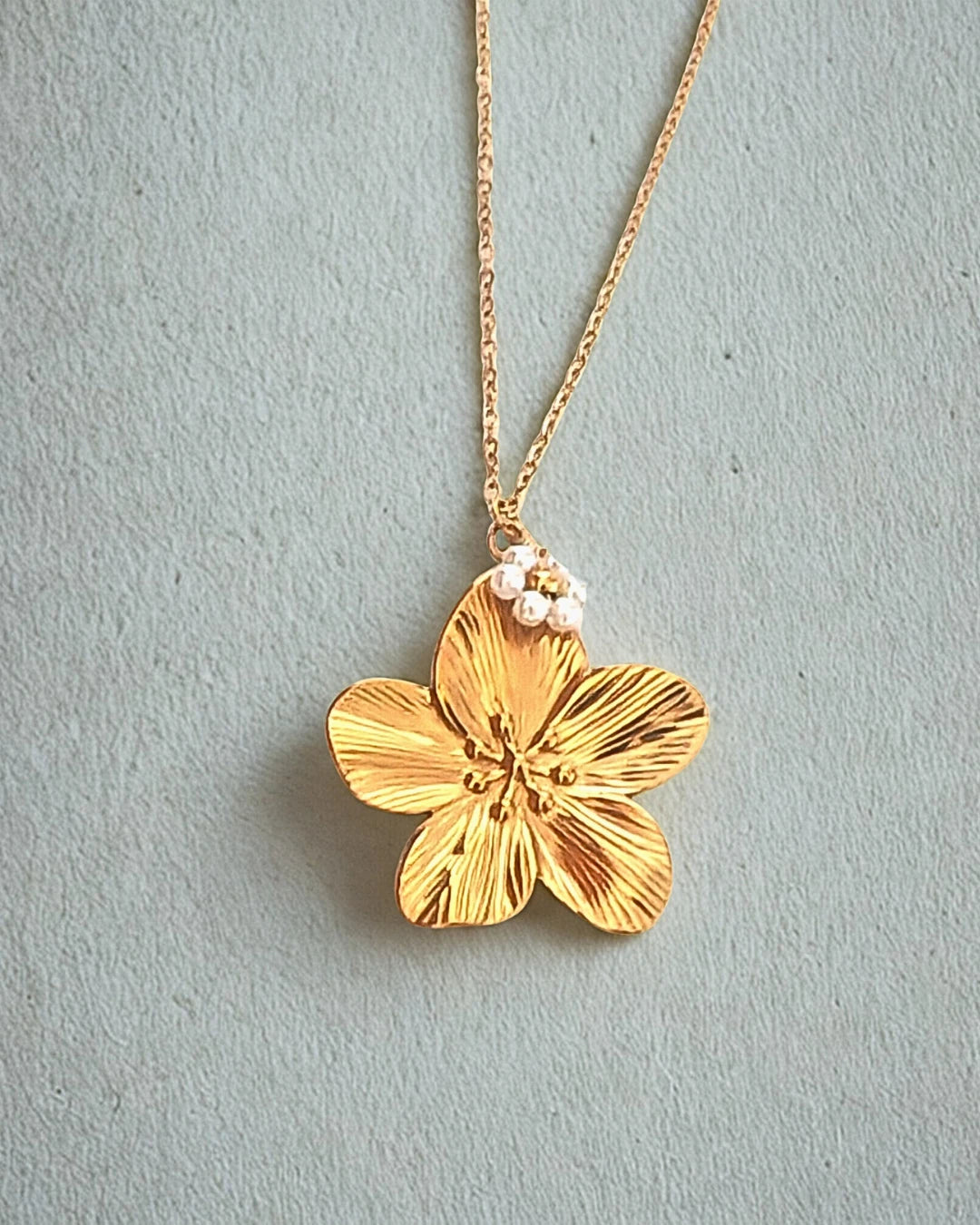 Laissez-vous séduire par la beauté de ce collier doré orné d’un pendentif en forme de fleur délicatement sculptée, rehaussée de petites perles nacrées. À la fois raffiné et lumineux, il incarne la douceur et la féminité dans toute sa splendeur.